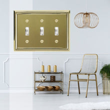 Load image into Gallery viewer, Decorative Contoured Metal "Estate" Bright Brass Triple Toggle Wall-plate in front of a bright white living room with brass furniture