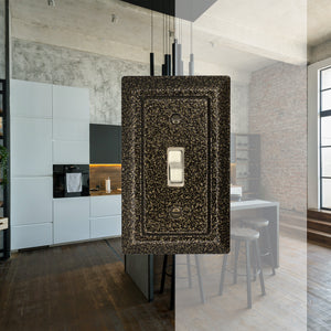 Decorative Metal Weathered Brass Single Toggle wall-plate in fron of a background image of a bright, modern, marble finished kitchen